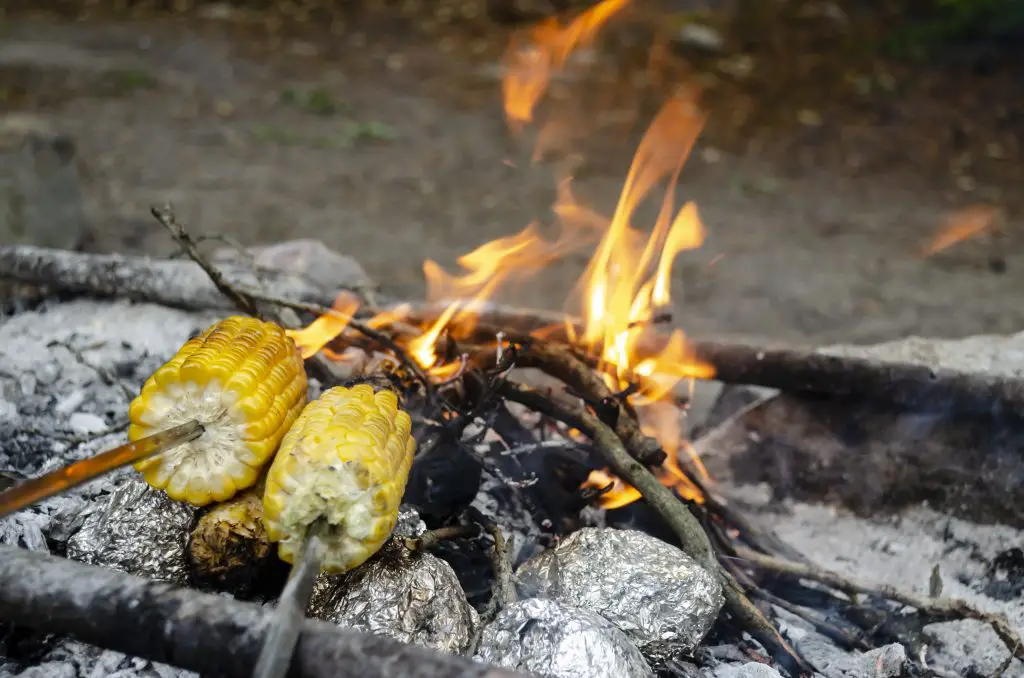 Two ears of corn roasting on the fire. The foil wrapped potatoes, which is prepared in the hot coals of the fire. Sweet Corn, Barbecue Fire