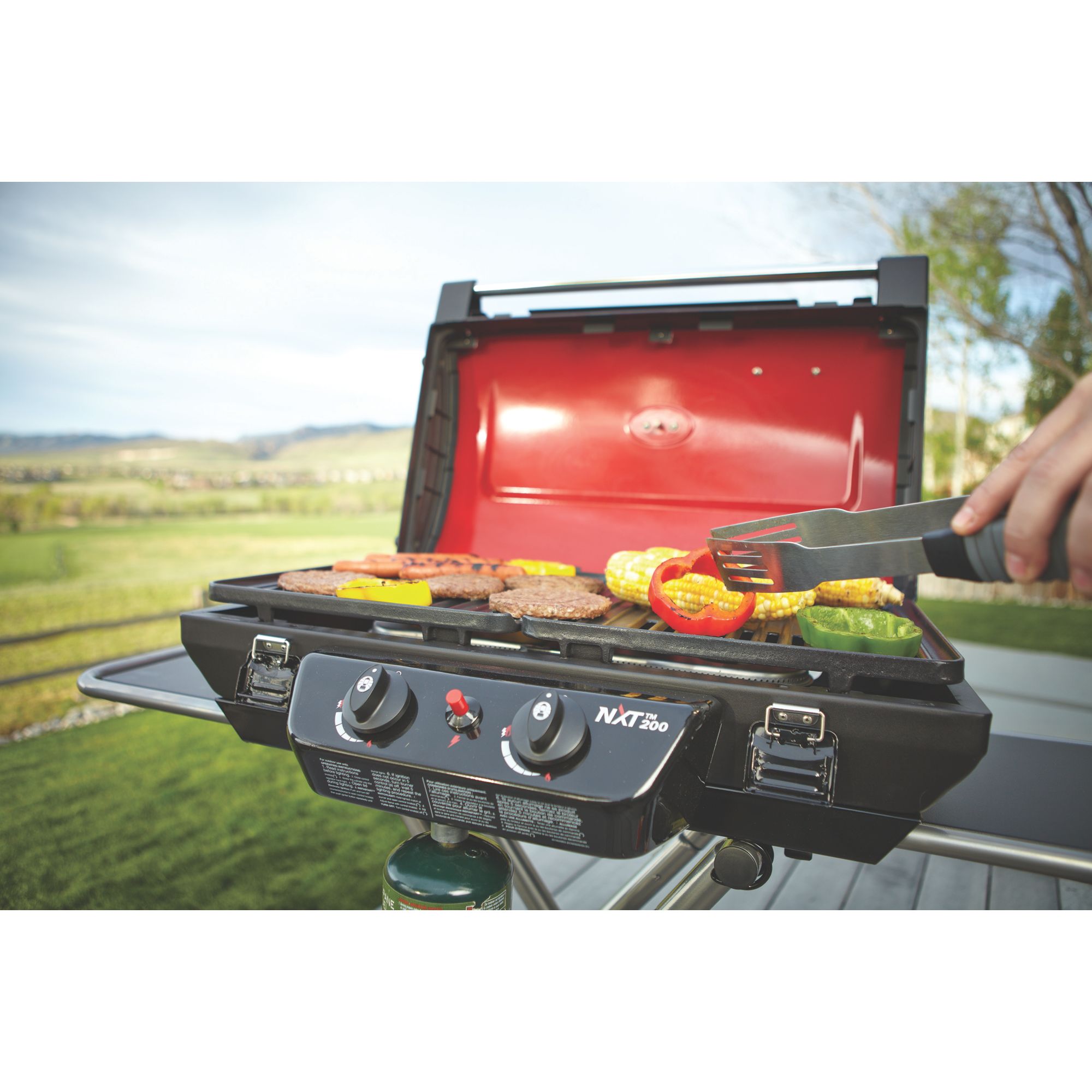 hamburgers, hotdogs, corn, and peppers on red Coleman grill