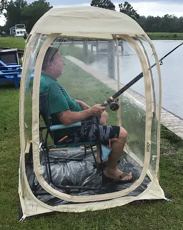 man in wheelchair fishing while sitting inside a clear pop up shelter