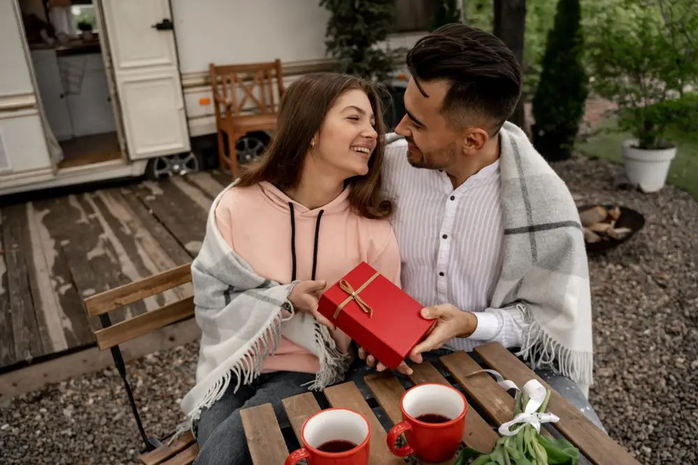 man presenting gift to happy woman near coffee on table in camping