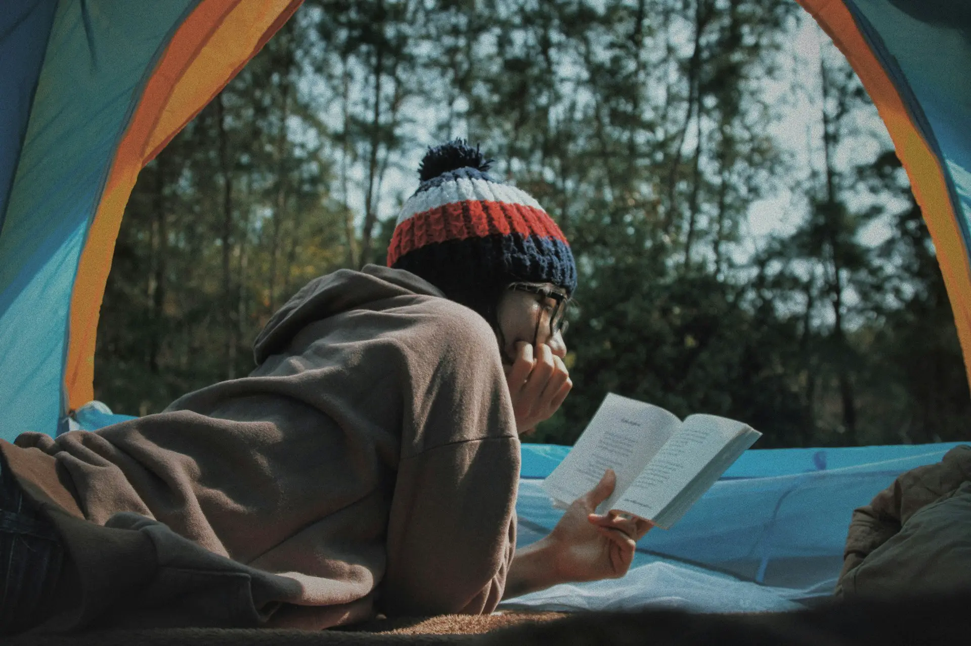 person with hat on inside a tent reading a book